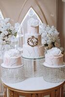 A large luxurious multi-tiered wedding cake is decorated with fresh white rose flowers in the banquet hall. Wedding dessert under the evening light. Wedding decor. photo