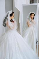 A young European woman with dark hair in a wedding dress stands by a mirror in a studio decorated with flowers. Young beautiful bride. photo