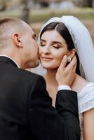 A young bride and groom tenderly embrace in the rays of the autumn sun. Tender and beautiful young girl bride. A man kisses his beloved. Against the background of a beautiful garden photo