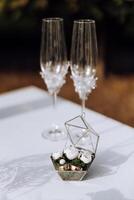 Wedding details. Gold wedding rings and champagne glasses are decorated with white buds. photo