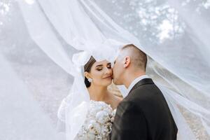 A young bride and groom tenderly embrace in the rays of the autumn sun. Tender and beautiful young girl bride. A man kisses his beloved. Against the background of a beautiful garden photo