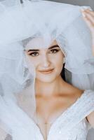 fashion photo of a beautiful bride with dark hair in an elegant wedding dress and stunning makeup in the room on the morning of the wedding. The bride is preparing for the wedding