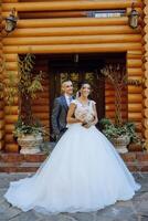 Stylish, young groom and beautiful bride in a long white dress and a long veil with a bouquet in their hands, hugging in the park in the autumn nature. Wedding portrait of newlyweds. photo