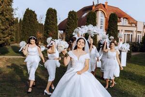 Wedding photography. The bride in a wedding dress and her friends in white dresses pose with bouquets near a white arch. photo