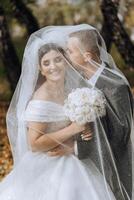 A young bride and groom tenderly embrace in the rays of the autumn sun. Tender and beautiful young girl bride. A man kisses his beloved. Against the background of a beautiful garden photo