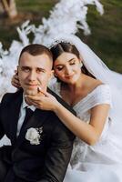 encantador y elegante recién casados son abrazando y sonriente en contra el antecedentes de otoño naturaleza en un hermosa jardín. un increíblemente hermosa joven novia inclinado en contra el hombro de su amado novio foto