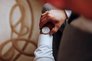 A close-up of a cropped frame of a man puts on a watch with a leather belt, is dressed in a stylish suit, a white shirt, wears a gold ring. photo