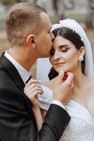 A young bride and groom tenderly embrace in the rays of the autumn sun. Tender and beautiful young girl bride. A man kisses his beloved. Against the background of a beautiful garden photo