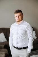 portrait of a young man in a white shirt and light pants in a room. The groom is preparing for the wedding photo