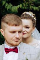 Portrait of a smiling bride with a bouquet of flowers hugging her husband while looking at the camera. Beautiful wedding celebration. Wedding hairstyle with a veil. Couple in love. photo