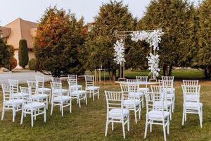 Decor at the wedding. Many white chairs and a golden arch decorated with white flowers photo