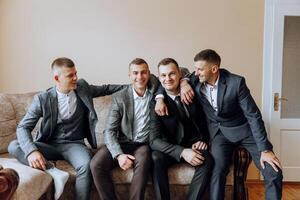 A young groom and his funny friends pose for the camera. A group of young people hug the groom and cheerfully congratulate him. Happy friends. Friends in the room. Wedding day. photo