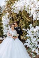 A young bride and groom tenderly embrace in the rays of the autumn sun. Tender and beautiful young girl bride. A man kisses his beloved. Against the background of a beautiful garden photo