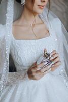 Glass bottle of perfume in gentle female hands. The bride sprays perfume on her body. Close-up photo. Manicure. Morning of the bride. photo