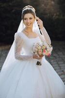 Portrait. A brunette bride in a dress and a veil, with a diadem, poses with a bouquet. Silver jewelry. Beautiful makeup and hair. Autumn wedding. celebration photo