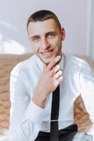 portrait of a young man in a white shirt and light pants in a room. The groom is preparing for the wedding photo