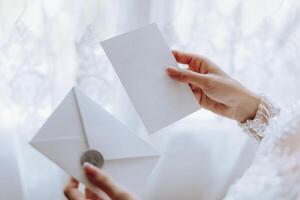 el novia en su manos sostiene un blanco sobre, un invitación, un regalo sábana de papel. de cerca Boda fotografía, Copiar espacio, retrato. foto