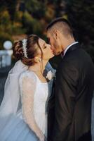 A young bride and groom tenderly embrace in the rays of the autumn sun. Tender and beautiful young girl bride. A man kisses his beloved. Against the background of a beautiful garden photo