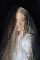 portrait of an incredibly beautiful girl bride in a white robe in the bedroom, the bride poses holding her veil in her hands and covers herself with it. photo