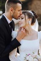 A young bride and groom tenderly embrace in the rays of the autumn sun. Tender and beautiful young girl bride. A man kisses his beloved. Against the background of a beautiful garden photo