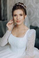 fashion photo of a beautiful bride with dark hair in an elegant wedding dress and stunning makeup in the room on the morning of the wedding. The bride is preparing for the wedding