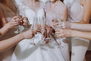 foto con damas de honor Bebiendo champán desde lentes en el Mañana en un hermosa hotel. foto de un hermosa joven novia y su amigos en pareo vestidos Bebiendo champán antes de el boda.