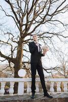 retrato de un hermoso joven novio en un otoño día al aire libre en un elegante traje y participación un Boda ramo de flores de flores al aire libre foto. hermoso hombre en un negocio traje. foto