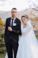 lovely and stylish newlyweds are hugging and smiling against the background of autumn nature in a beautiful garden. An incredibly beautiful young bride leaned against the shoulder of her beloved groom photo