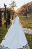 A blonde bride in a white dress with a long train holds the dress and walks along the stone path. Autumn. Wedding photo session in nature. Beautiful hair and makeup. celebration