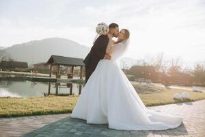 A young bride and groom tenderly embrace in the rays of the autumn sun. Tender and beautiful young girl bride. A man kisses his beloved. Against the background of a beautiful garden photo