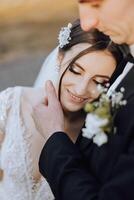 Portrait of a smiling bride with a bouquet of flowers, embracing her husband, with her eyes closed. Nice wedding celebration. Wedding hairstyle with a veil. Couple in love. photo