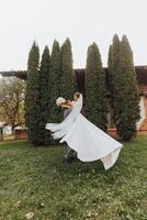 Handsome groom carrying a beautiful laughing bride in his arms in a spring park. The groom is circling with the bride in his arms photo