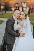 Stylish, young groom and beautiful bride in a long white dress and a long veil with a bouquet in their hands, hugging in the park in the autumn nature. Wedding portrait of newlyweds. photo