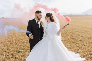 Wedding photo session in nature. Bride and groom look at each other, hold colored smoke