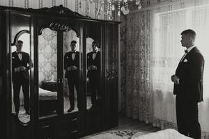 black and white photo. A handsome man in a black suit poses in front of the camera, reflected in the mirror. Side view. Daylight. Fashion and style. Business. Men's style. Beautiful hands photo