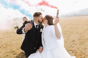 Wedding photo session in nature. Bride and groom kissing and holding colored smoke