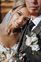 Portrait of a smiling bride with a bouquet of flowers hugging her husband while looking at the camera. Beautiful wedding celebration. Wedding hairstyle with a veil. Couple in love. photo