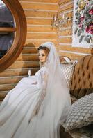 beautiful bride in a wedding dress with a beautiful hairstyle in a beautiful wooden interior, sitting on a luxurious sofa photo