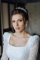 fashion photo of a beautiful bride with dark hair in an elegant wedding dress and stunning makeup in the room on the morning of the wedding. The bride is preparing for the wedding