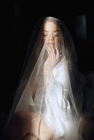 portrait of an incredibly beautiful girl bride in a white robe in the bedroom, the bride poses holding her veil in her hands and covers herself with it. photo