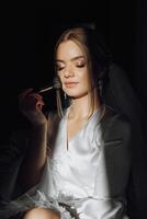 Happy mature girl bride in the bedroom under the rays of light in front of the mirror, applying makeup on her face photo