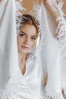 portrait of an incredibly beautiful girl bride in a white robe in the bedroom, the bride poses in the morning before the wedding ceremony. photo