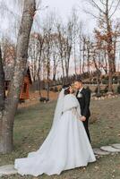 A young bride and groom tenderly embrace in the rays of the autumn sun. Tender and beautiful young girl bride. A man kisses his beloved. Against the background of a beautiful garden photo