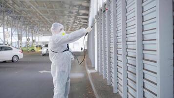 a man in a protective suit and mask with a water spraying tool is spraying the disinfectant in the parking lot video