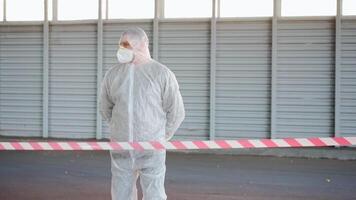 a person in a white protective suit and mask showing people to not pass the red line video