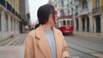 a woman in glasses and coat in a city is smiling to the camera video