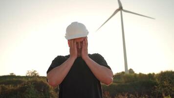 ein Mann im ein schwer Hut stellen Hand auf seine Gesicht im Vorderseite von ein Wind Turbine video