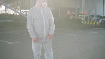 a man in a protective suit and mask with a water spraying tool standing in a parking lot video