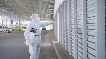 a man in a protective suit and mask with a water spraying tool is spraying the disinfectant in the parking lot video