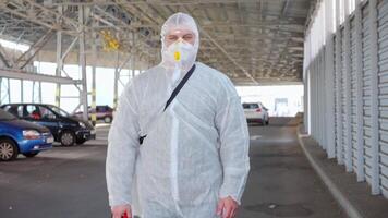 une homme dans une protecteur costume et masque avec une l'eau pulvérisation outil en marchant dans un vide parking lot video